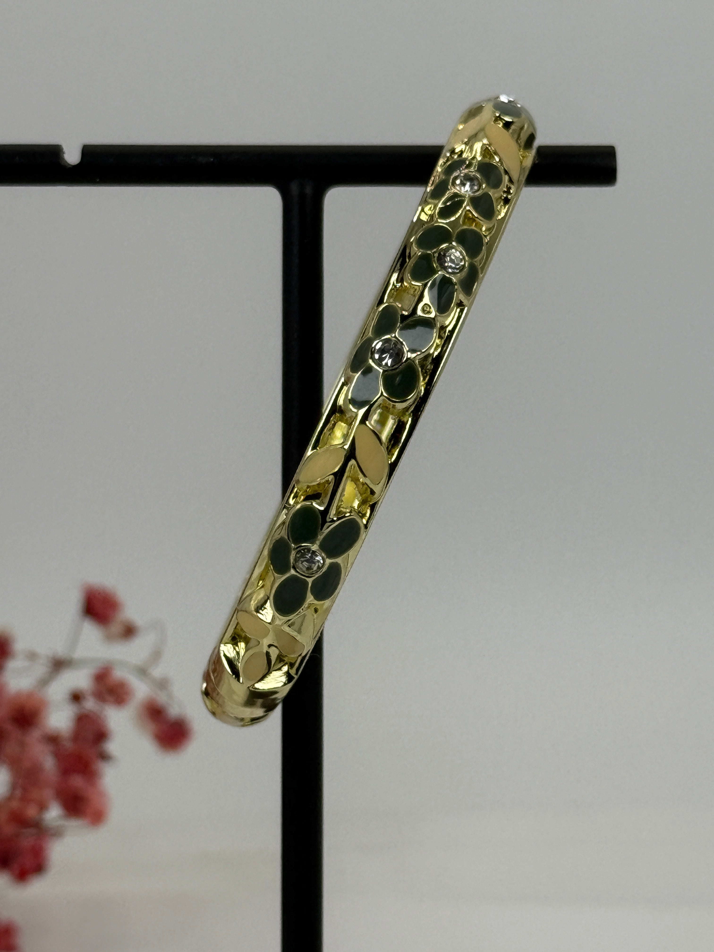 Scharnierende messing vergulde armband met groen en geel geëmailleerd bloemmotief – binnendiameter 6 cm.