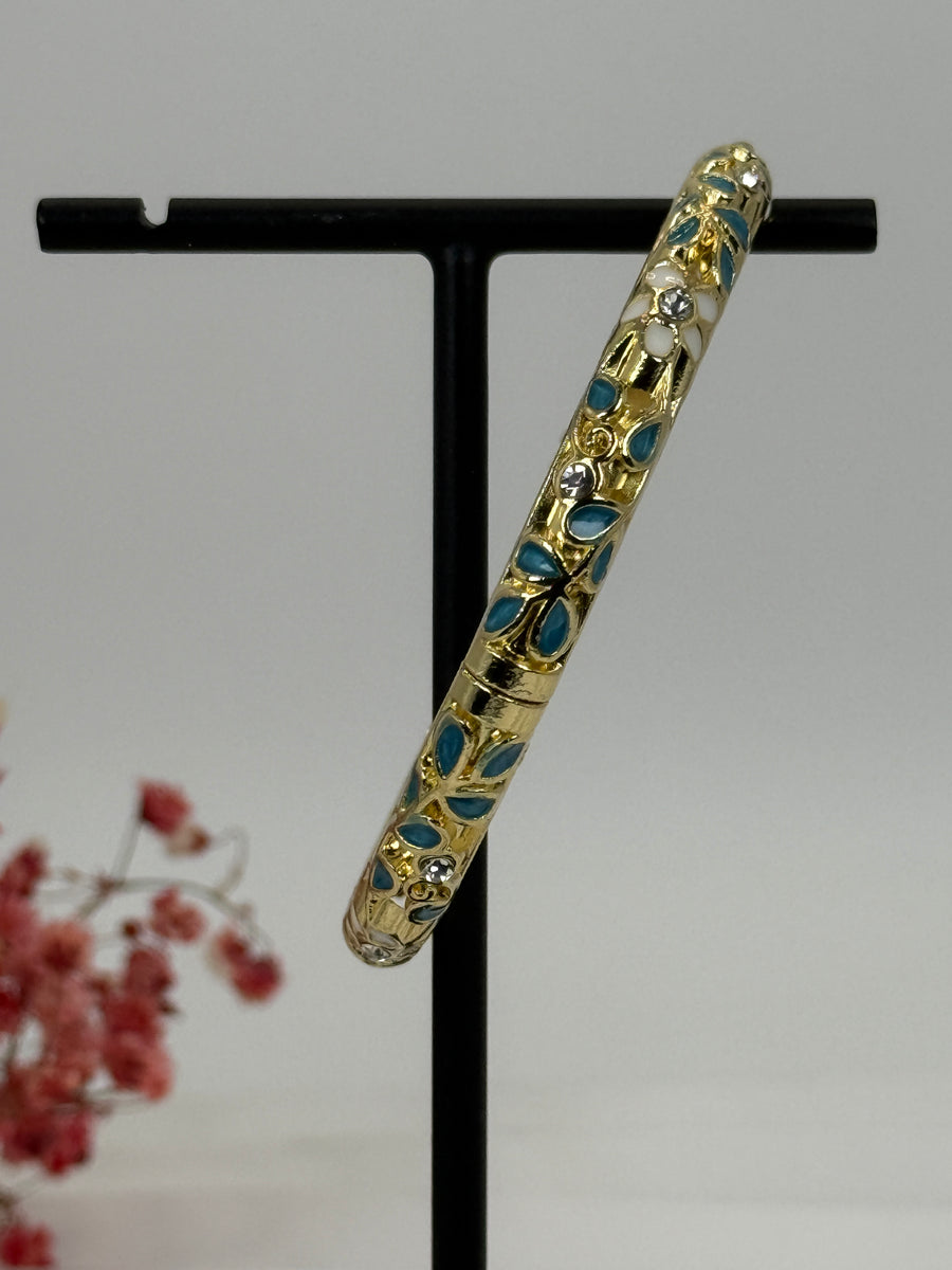 Armreif, aufklappbar, aus vergoldetem Messing, emailliertes Blumenmotiv in Blau (1) und Weiß – Innendurchmesser 6 cm.