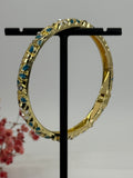 Open bRASSLET met vergulde, blauw (1) en wit geëmailleerd bloemmotief – binnendiameter 6 cm.