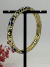 Aufklappbarer Armreif aus vergoldetem Messing mit floralem Muster in blauem (3) und weißem Emaille – Innendurchmesser 6 cm.