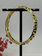 Opengaande messing bangle armband met vergulde, zwart-wit geëmailleerde bloemmotieven – binnendiameter 6 cm.