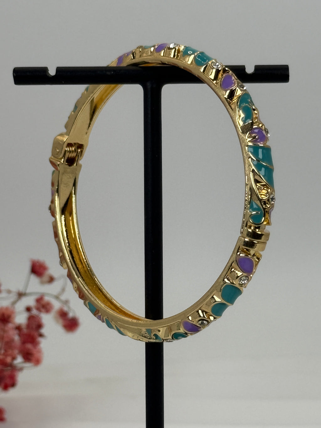 Gouden, opengaande messing armband met groen en paars geëmailleerd bloemmotief – binnendiameter 6 cm.