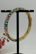 Gouden, opengaande messing armband met groen en paars geëmailleerd bloemmotief – binnendiameter 6 cm.