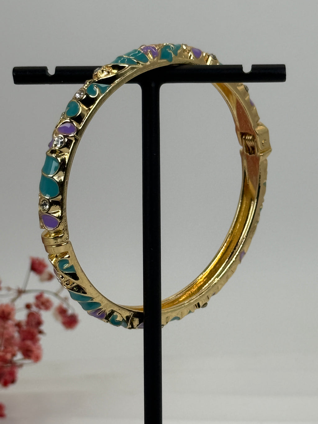Gouden, opengaande messing armband met groen en paars geëmailleerd bloemmotief – binnendiameter 6 cm.