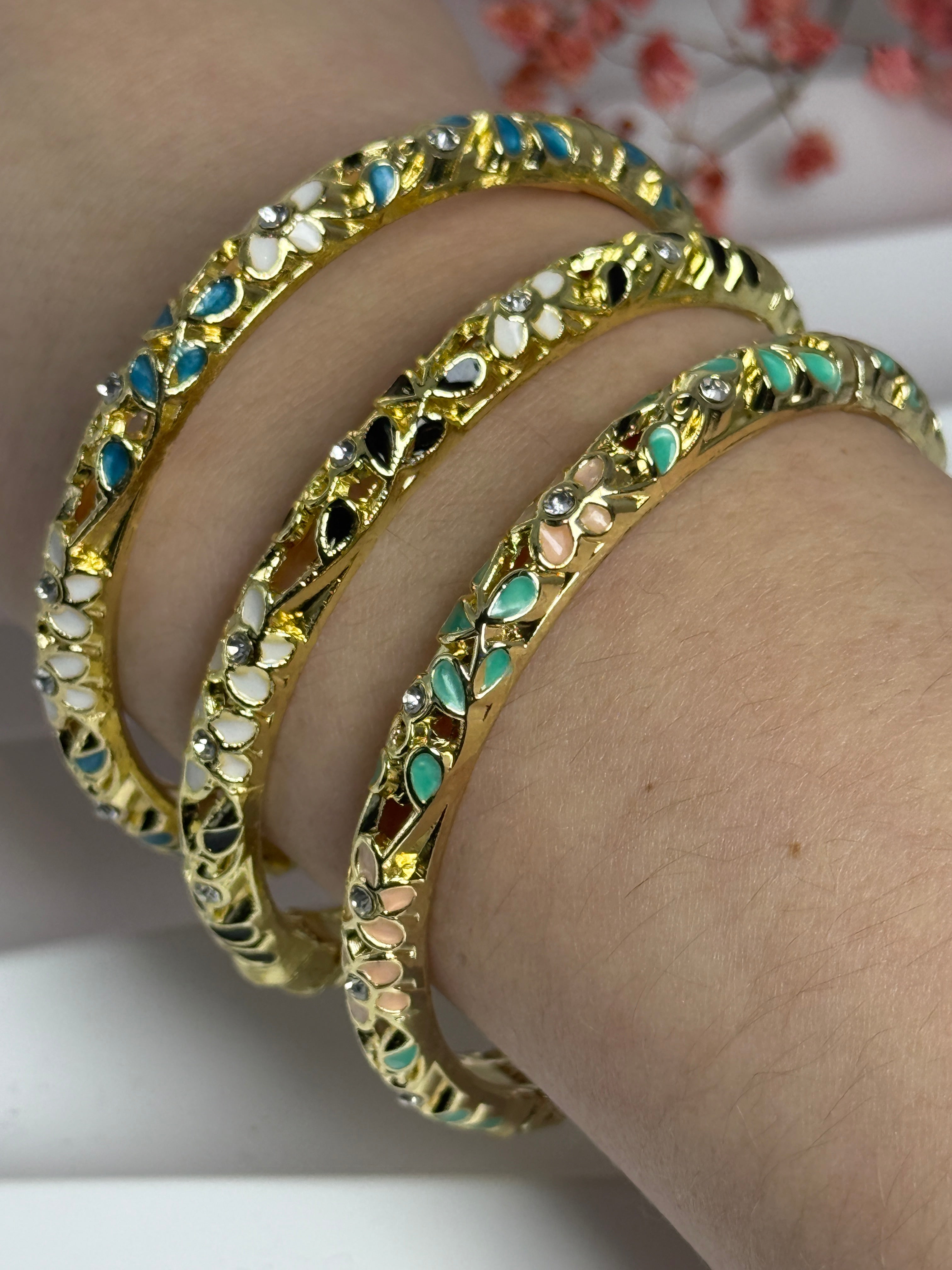 Goudkleurige messing openslaande bangle met geëmailleerd bloemmotief in groen en roze – binnendiameter 6 cm.